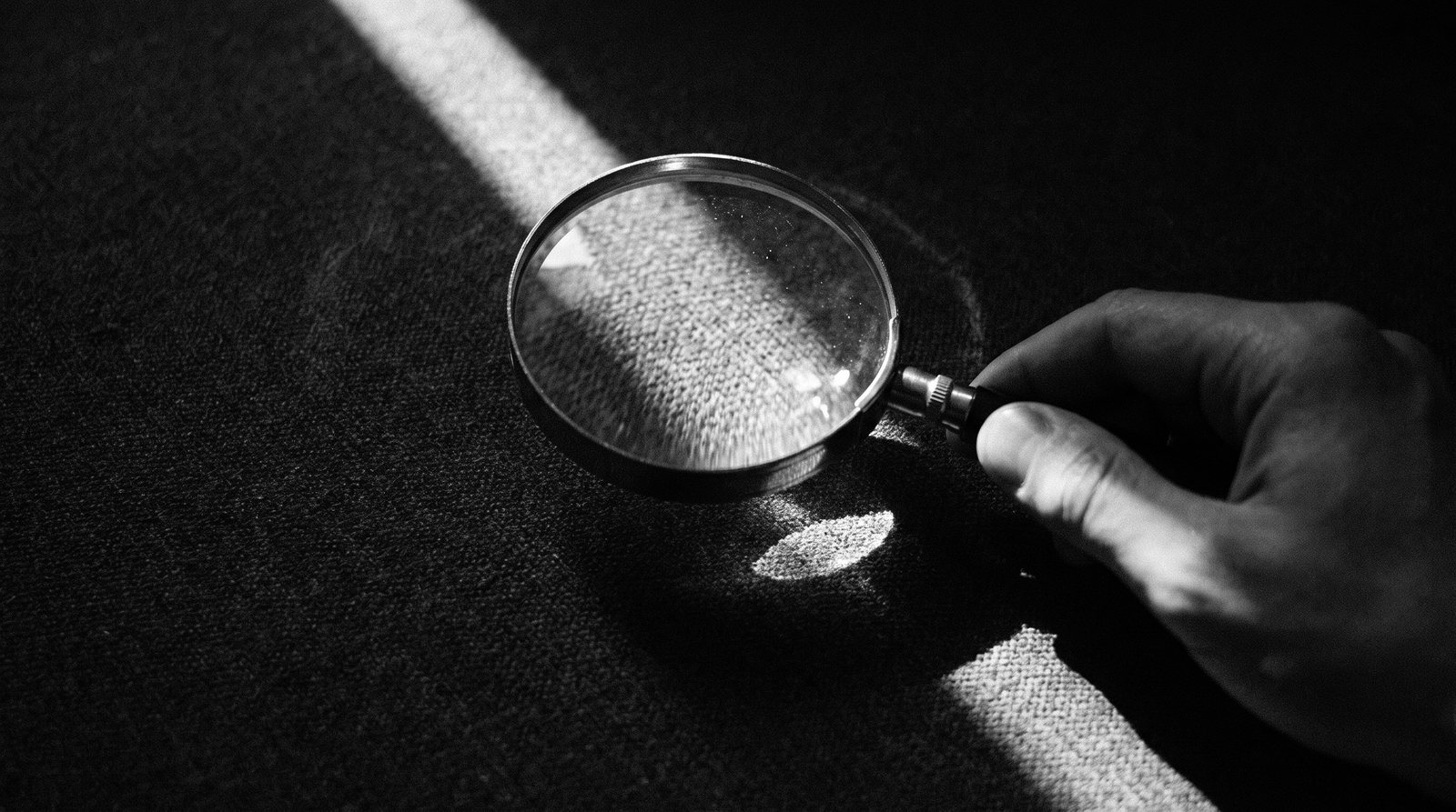 A magnifying glass held over a dark textured surface catching a sliver of light