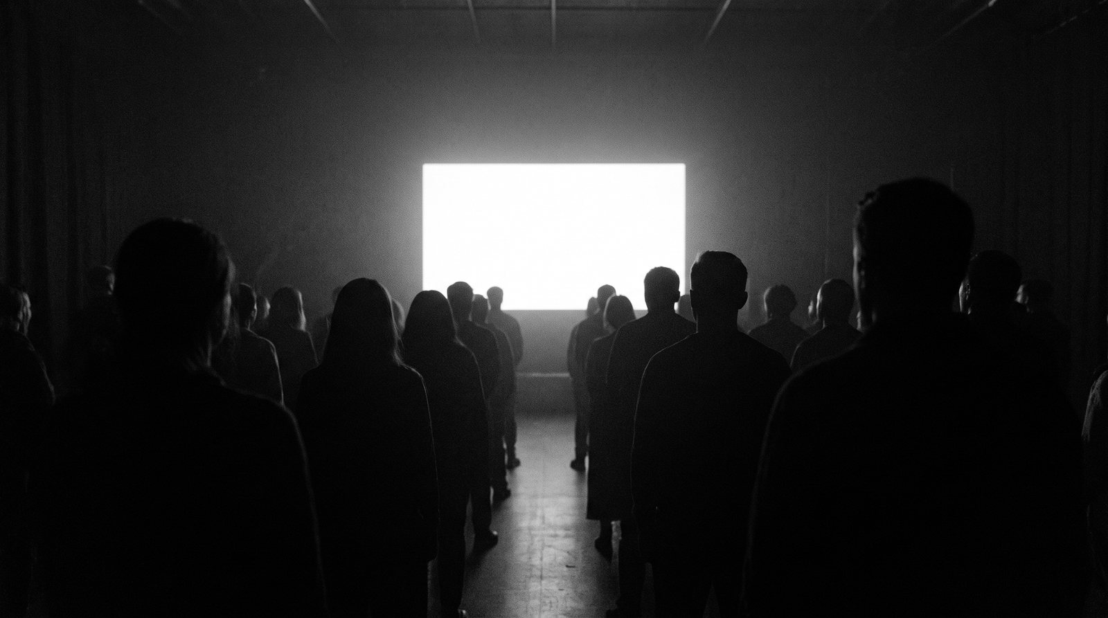 A crowd of faceless silhouettes facing a distant glowing screen in the dark