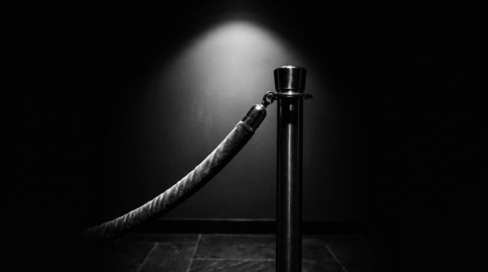 A single stanchion post with a velvet rope in near-darkness